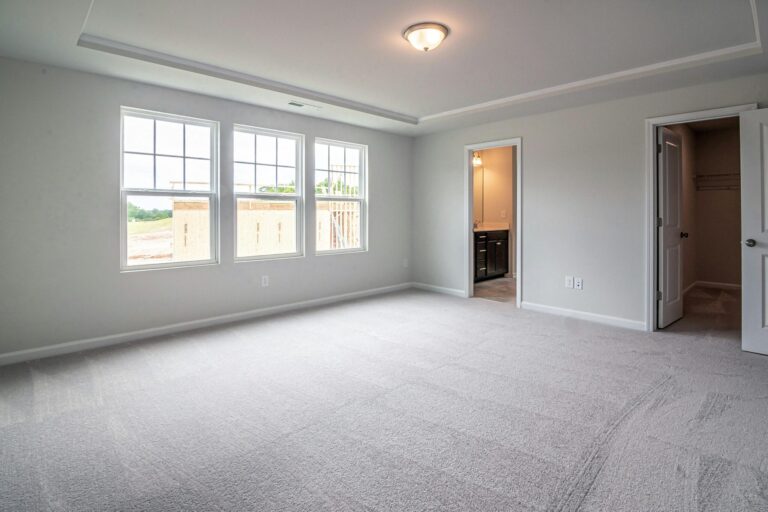 Interior view of a spacious modern bedroom with large windows and carpeted flooring